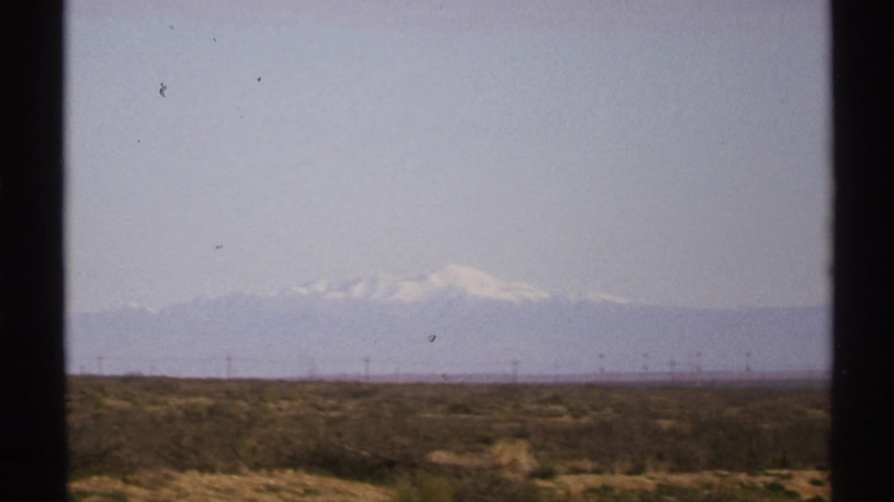 Hazy desert plain with power lines and pale snow-capped mountains on the horizon.