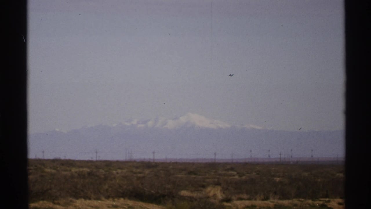 Desert scrubland with distant snow-capped mountains under a hazy sky.