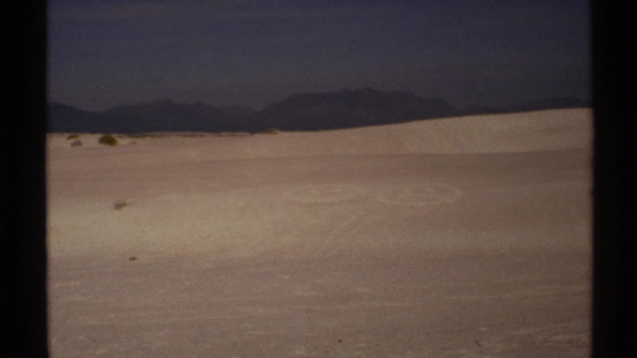 Pale sand dunes with dark mountains in the distance.