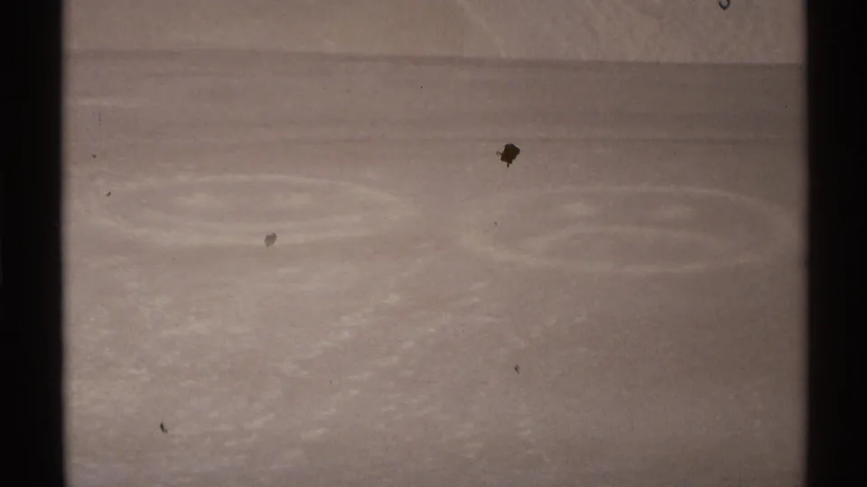 1972 New Mexico 8mm frame showing a pale sand or snow-like surface with faint circular impressions under a dark blue sky.