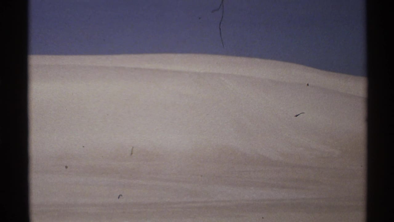 Pale ridge or dune-like surface under a dark sky, with film dust visible.