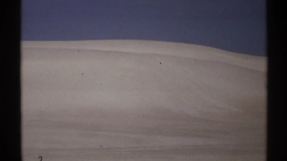 1972 New Mexico 8mm frame showing a low, pale sand or snow-like slope with faint bands and a dark blue sky.