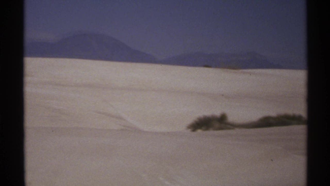 Rolling white dunes, low shrubs, and distant mountain silhouettes.