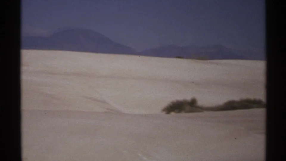 1972 New Mexico 8mm view of rolling white sand with sparse vegetation and mountains along the far horizon.