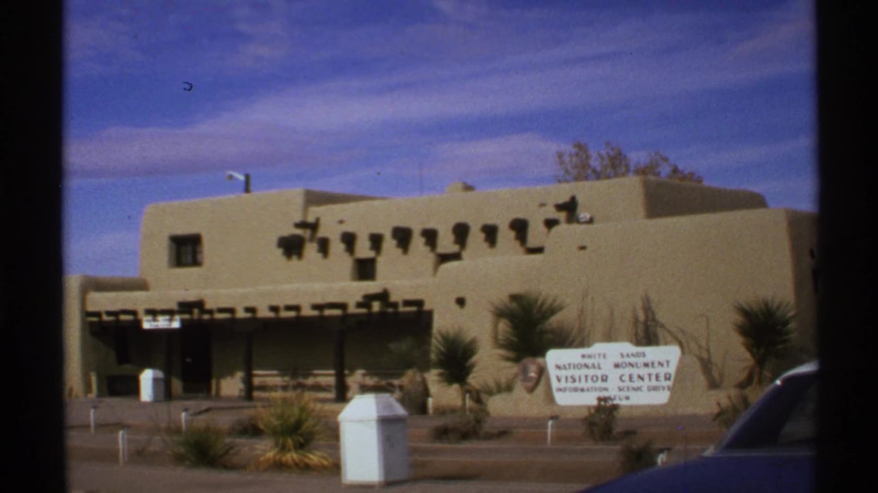 1972 8mm view of the White Sands National Monument Visitor Center exterior in New Mexico under a blue sky.