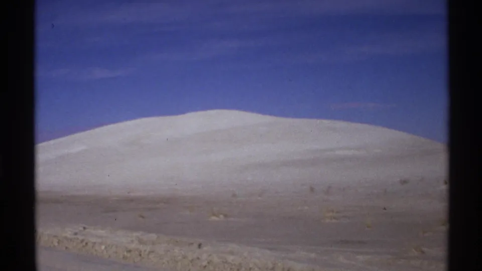 1972 New Mexico 8mm frame with a broad white dune, sparse desert plants, and an uninterrupted blue sky.