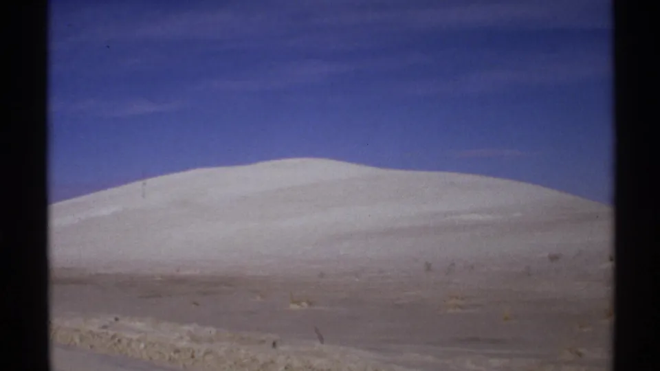 1972 New Mexico 8mm frame showing the dune slope closer in, with sparse scrub and visible film grain.
