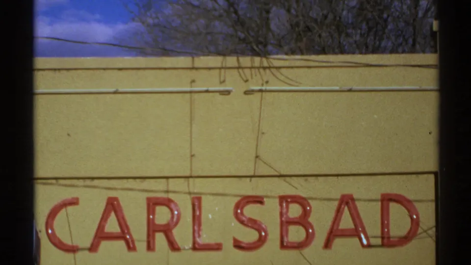 1972 New Mexico 8mm frame centered on red CARLSBAD letters across a yellow building facade under bare trees and blue sky.