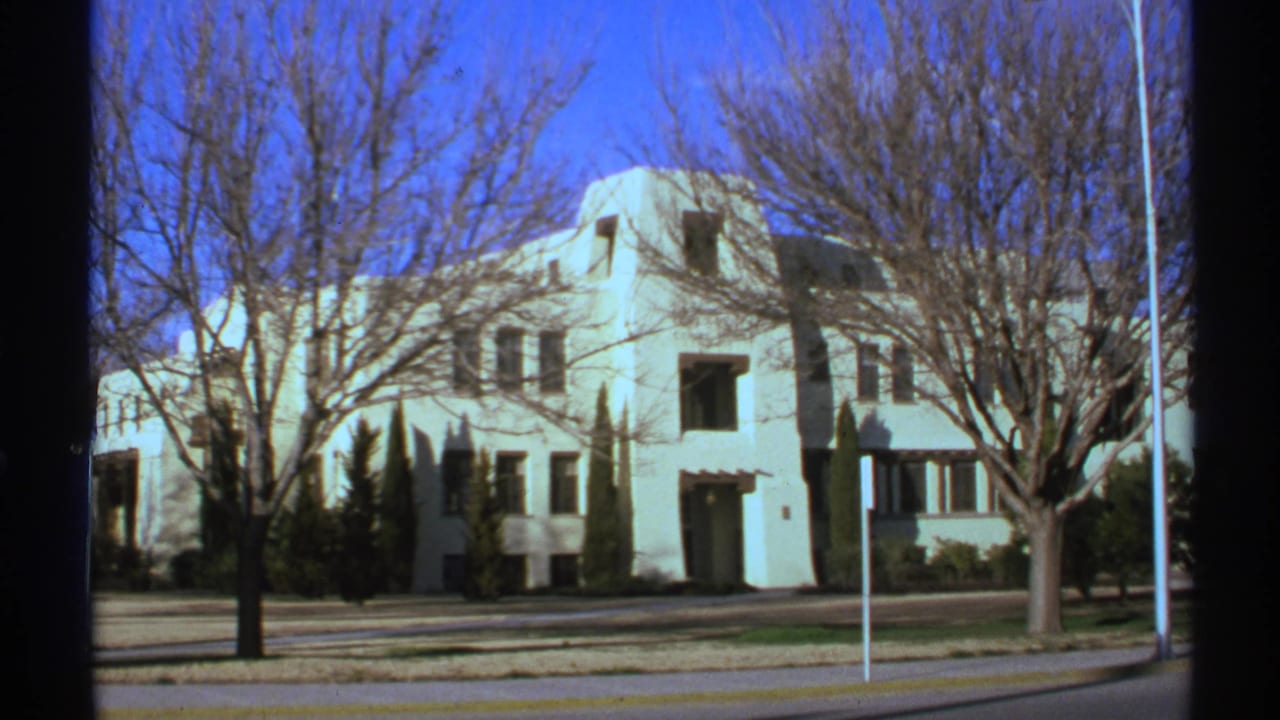 1972 New Mexico 8mm frame showing a large white building with square and rectangular windows viewed from across a street.