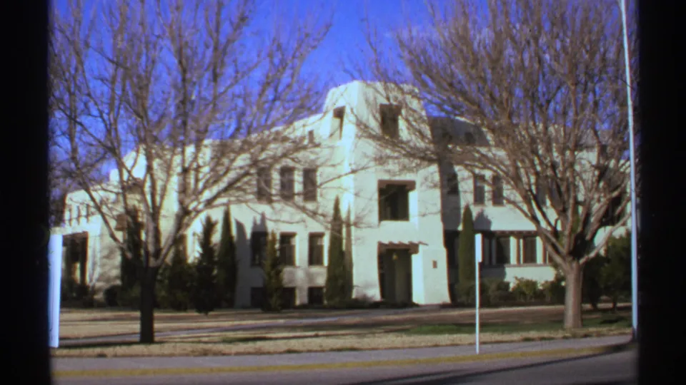 A slightly shifted 1972 8mm frame shows the white building, bare trees, sidewalk, and roadway in bright daylight.