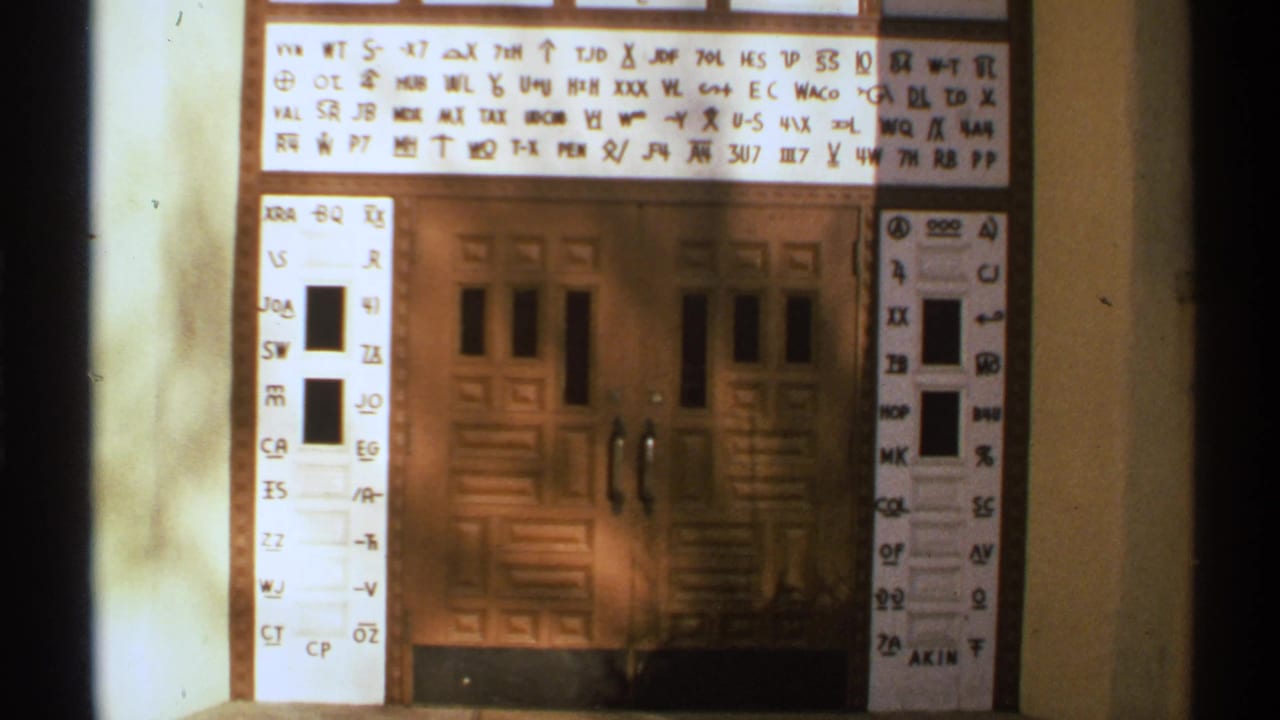 1972 New Mexico 8mm frame showing a white symbol-and-letter sign mounted above brown wooden double doors.