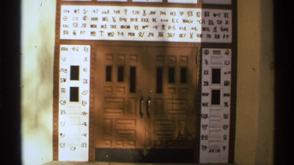 1972 New Mexico 8mm frame showing a white symbol-and-letter sign mounted above brown wooden double doors.
