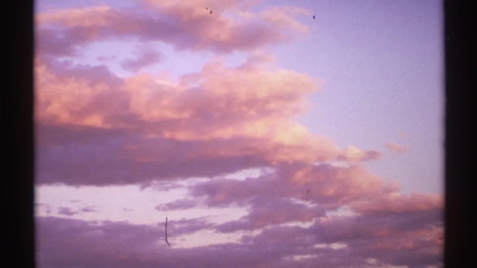 1972 New Mexico sunset frame showing pink, lavender, and purple clouds across a twilight sky, with visible 8mm grain and gate borders.