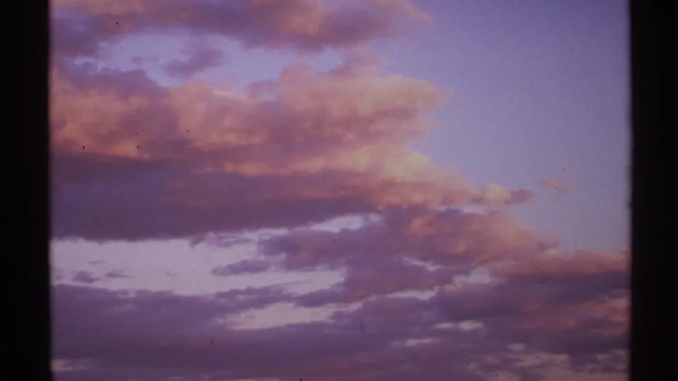 1972 New Mexico 8mm frame showing layered purple and red dusk clouds, dark sky bands, grain, and visible film edges.