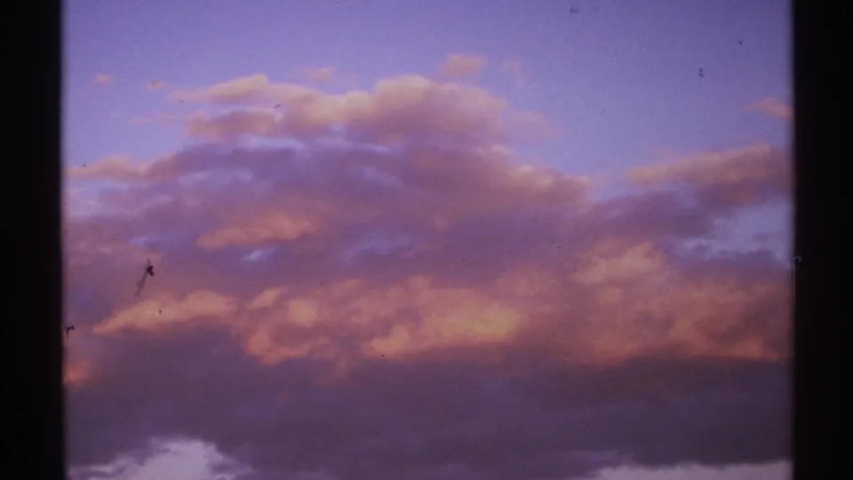 1972 New Mexico 8mm frame showing soft dusk clouds in purple, orange, and blue tones with visible grain and light surface marks.