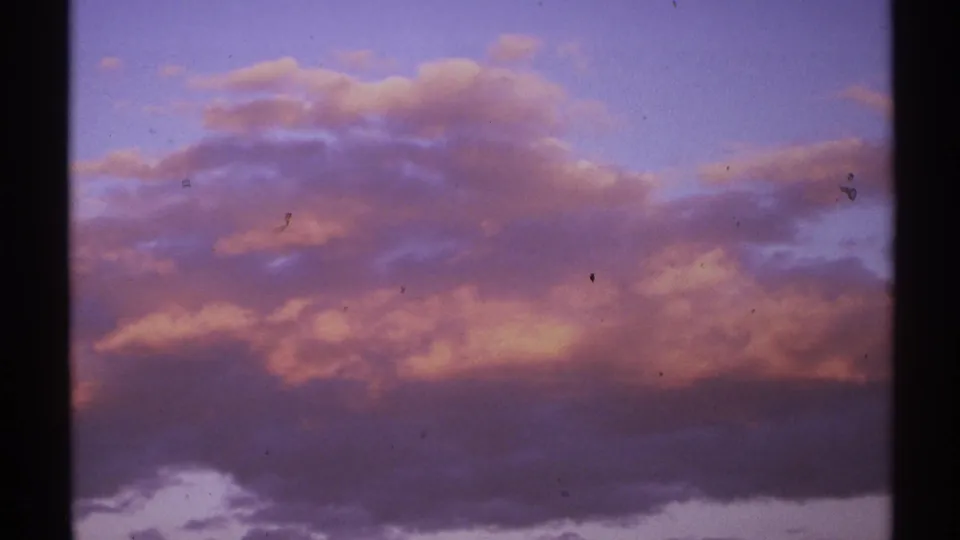 1972 New Mexico 8mm frame of a red-purple cloud bank beneath blue dusk sky, with grain, dust specks, and dark film borders visible.