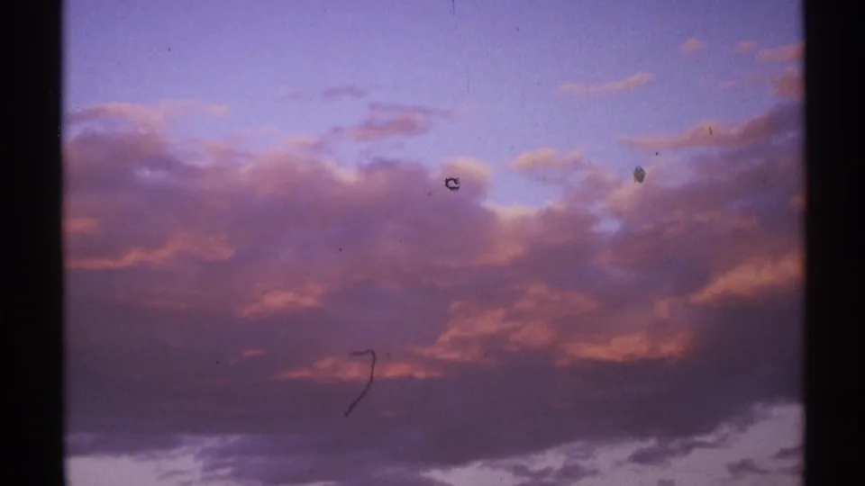 1972 8mm footage shows a low cloud bank at sunset, with pink color shifts, dust, and light scratches visible in the scan.
