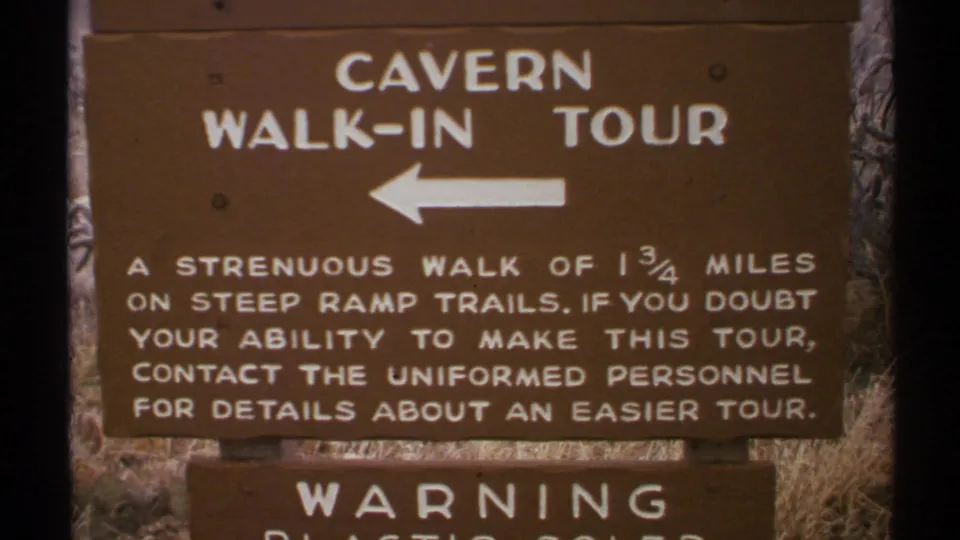 New Mexico 1972 home-movie frame showing a brown Cavern Walk-In Tour sign with white text, a left arrow, and a warning panel below.