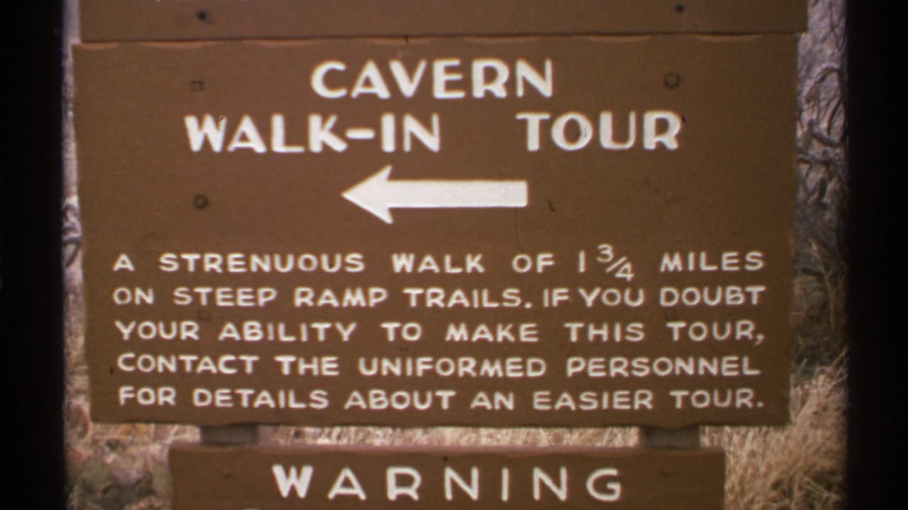 Brown cavern walk-in tour sign with a left arrow and warning text below.