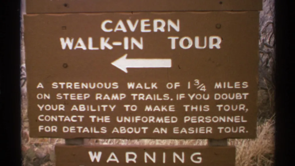 1972 New Mexico 8mm frame showing a brown cavern walk-in tour sign with white lettering, a left arrow, and a partial warning placard.