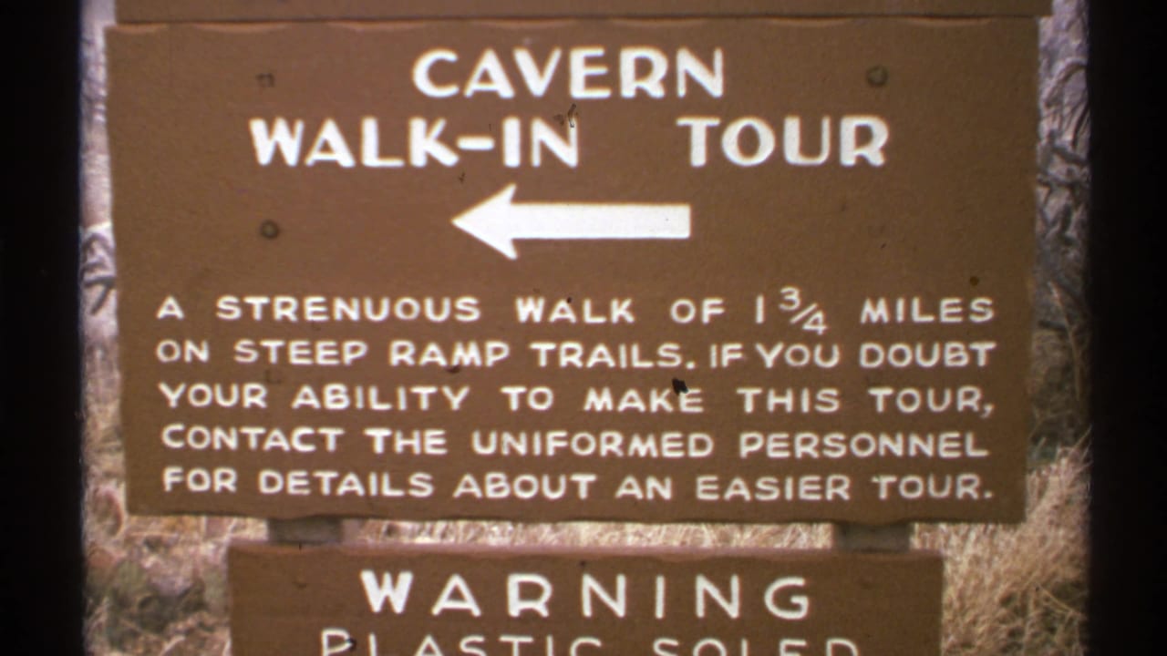 1972 New Mexico frame of the cavern walk-in tour sign, with white arrow and visitor guidance about steep ramp trails and an easier tour.