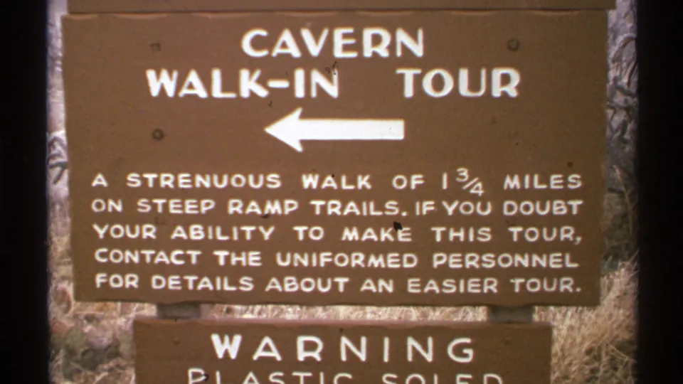 1972 New Mexico frame of the cavern walk-in tour sign, with white arrow and visitor guidance about steep ramp trails and an easier tour.