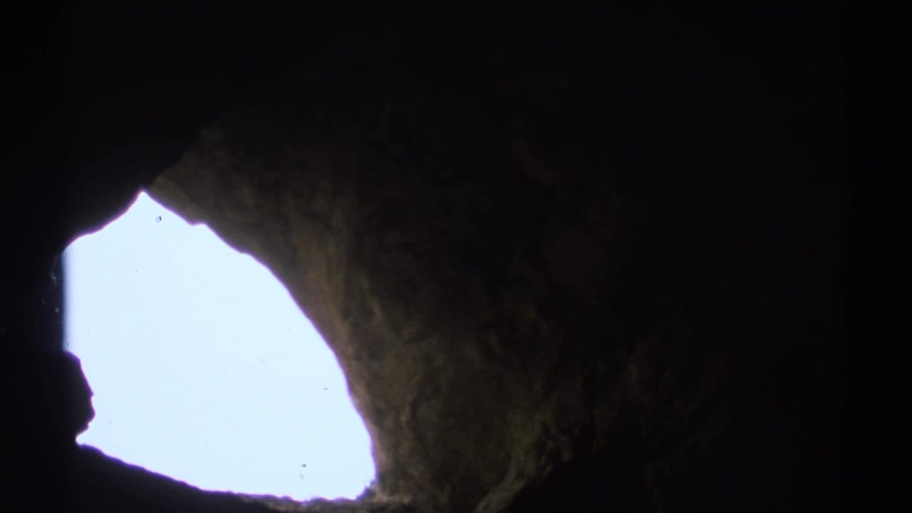 Dark cavern interior framing a bright irregular opening to the sky.