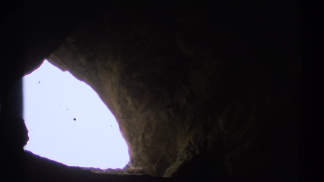 Bright cave opening surrounded by dark, rough rock walls.