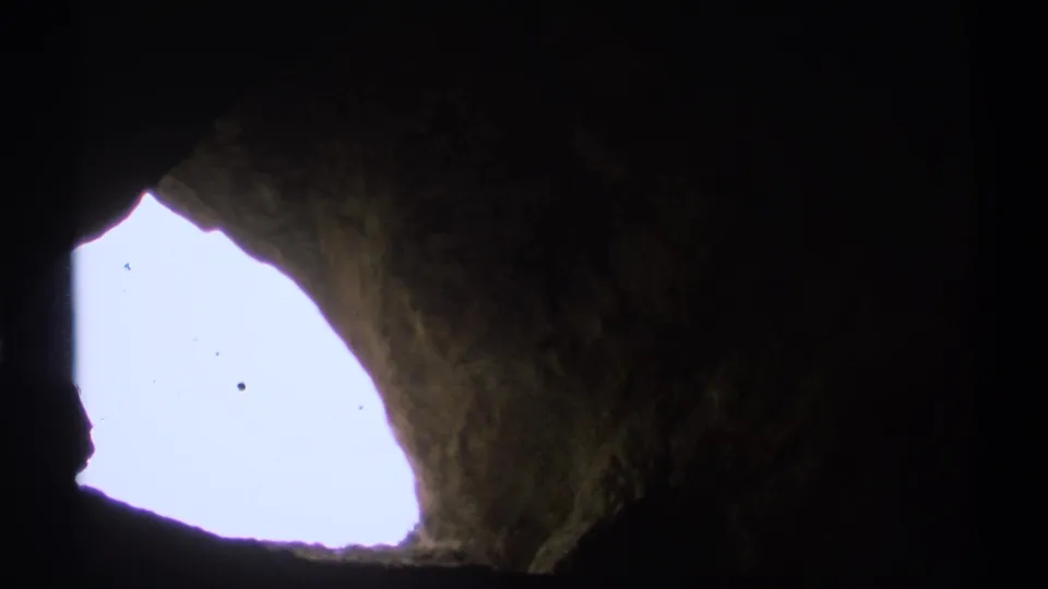 A visitor-shot 8mm view from inside the cavern, with the opening blown out by sunlight and rock walls in silhouette.