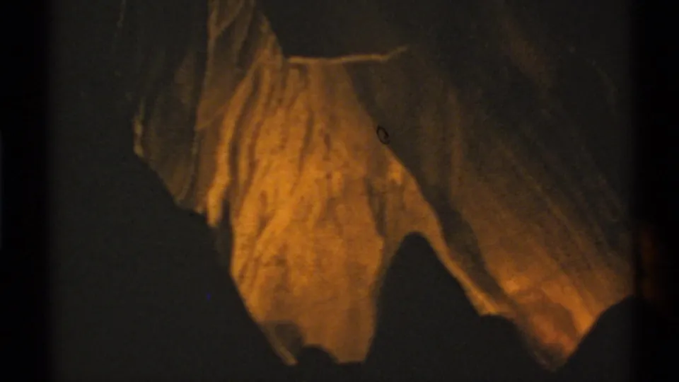 1972 New Mexico 8mm frame showing amber-lit hanging rock forms inside a dark cave interior.