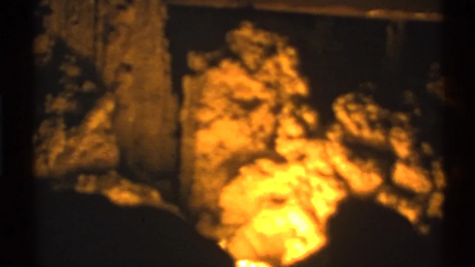 1972 8mm cave view with a stone column, rough floor, and bright amber light in the foreground.