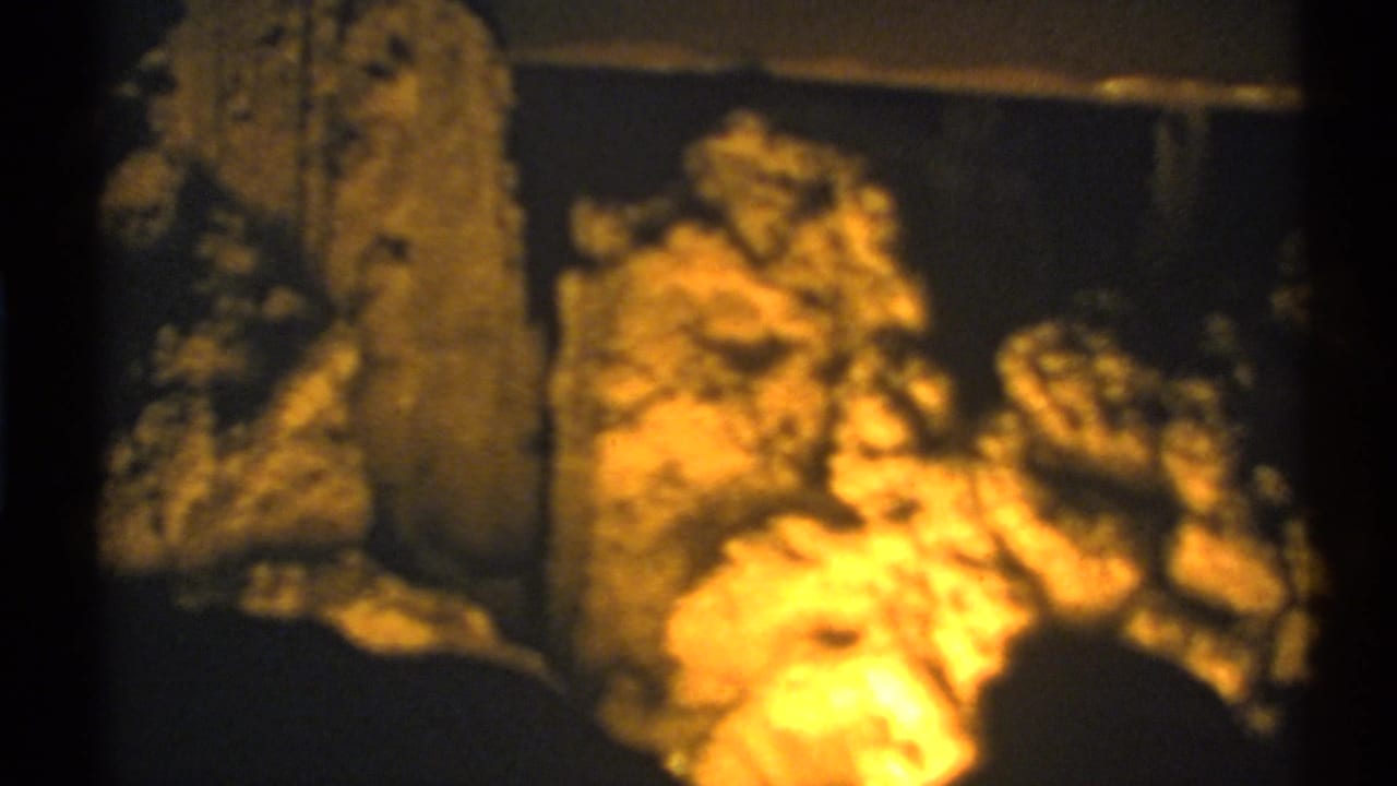 Dim cave interior with warm light on rough rock formations and deep surrounding shadow.