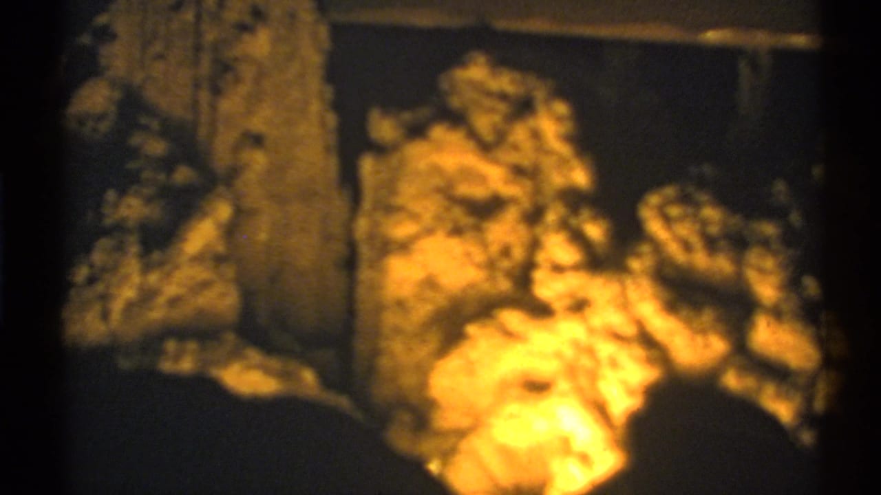 1972 New Mexico cave view with illuminated stone clusters and a darker vertical formation in the foreground.