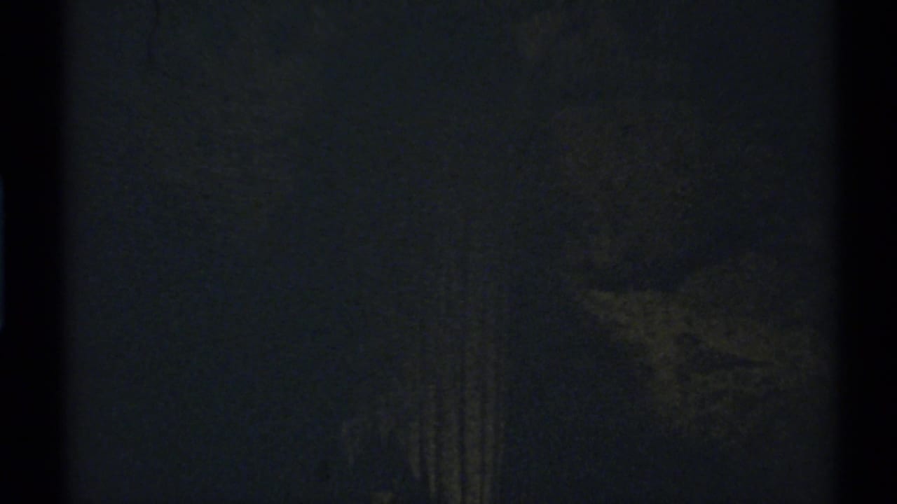 Very dark interior frame with a faint vertical column-like form near the center.