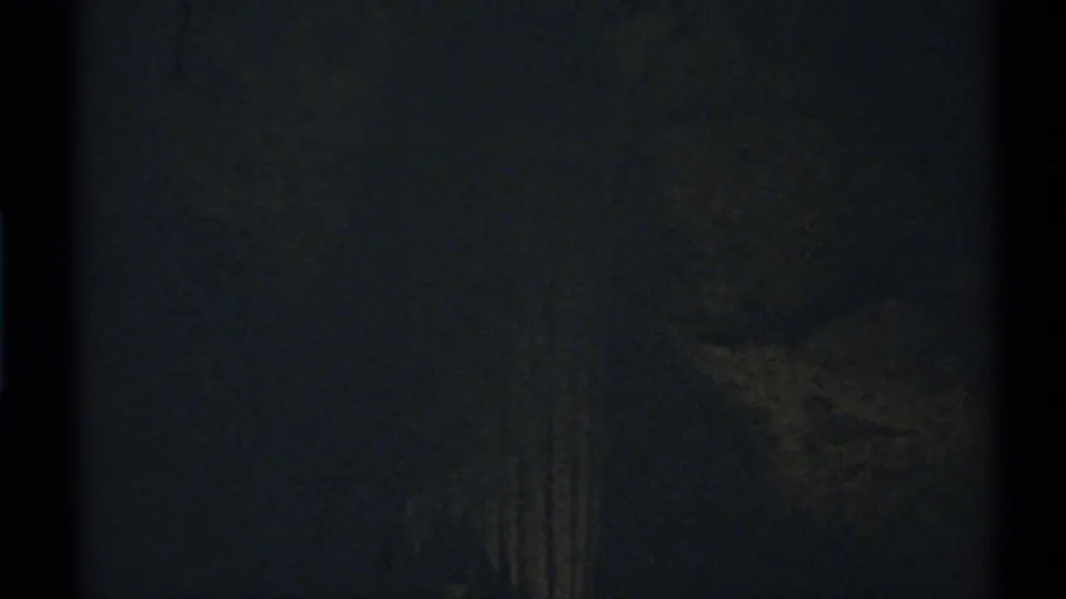 Dark 1972 New Mexico 8mm frame with a barely visible vertical decorative form in a shadowed interior.