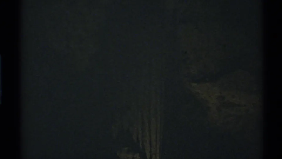 Grainy 1972 New Mexico home-movie frame showing a dim vertical interior detail against deep shadow.