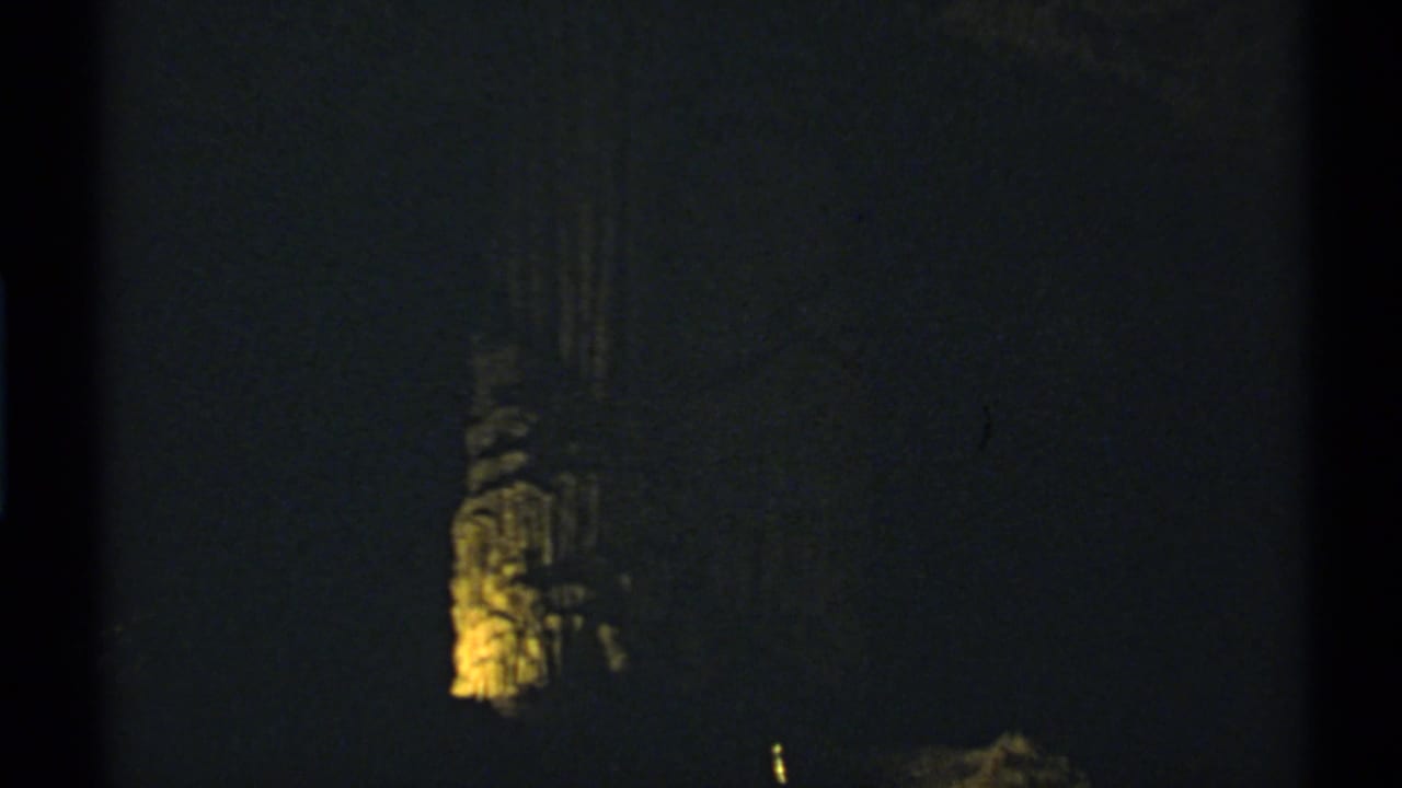 Dark cave interior with a warm-lit vertical rock formation near the left side.