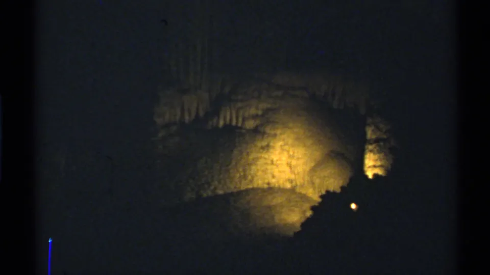 1972 New Mexico 8mm frame showing a larger cave formation glowing in yellow light, with layered mineral deposits visible above.