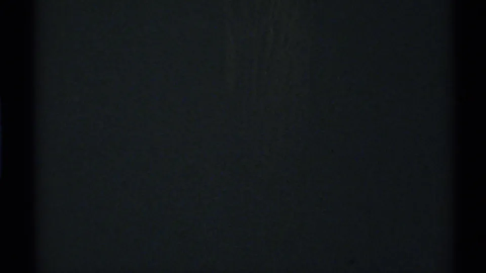 Nearly black 8mm frame with faint vertical tonal variation, grain, and dark side edges, with no identifiable people or setting visible.