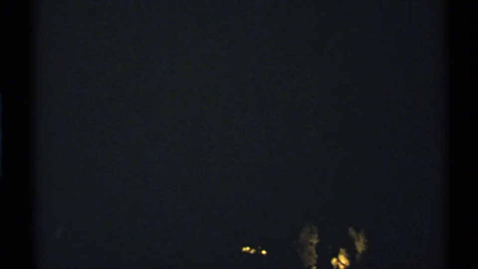 1972 New Mexico 8mm night frame with faint distant yellow-white lights in an otherwise dark, grainy scene.