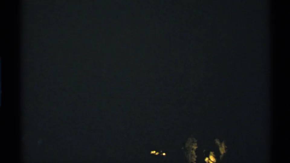 Grainy 1972 New Mexico nighttime frame with faint lights and indistinct pale forms in the lower right area.