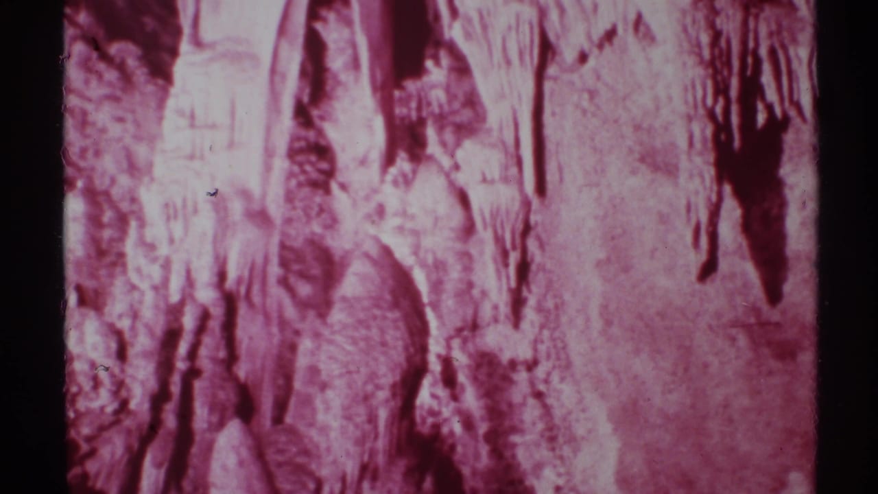 Pink-tinted cave wall with stalactites and rough mineral formations.