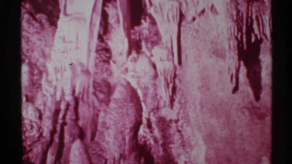 1972 8mm New Mexico cave interior with pink-tinted stalactites, rough rock textures, and dark recesses.