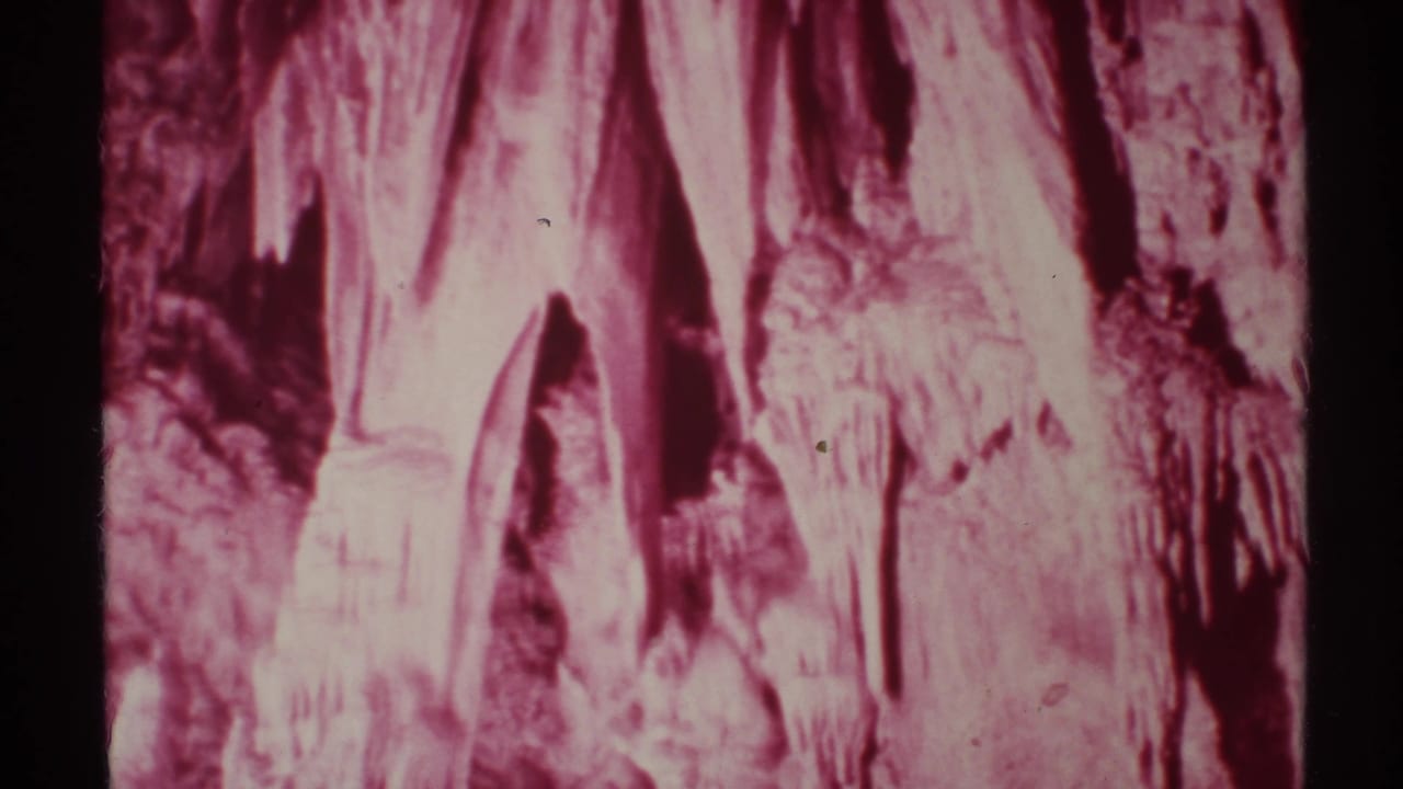 Reddish 8mm frame of stalactites hanging from a cave ceiling.