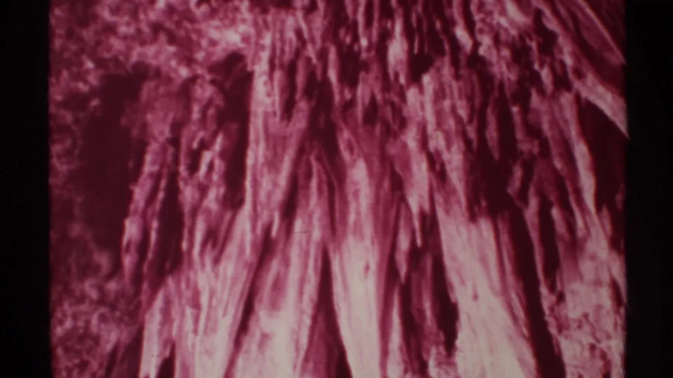Close-up of red-lit cave textures and stalactite-like forms, with visible 8mm grain and frame edge.