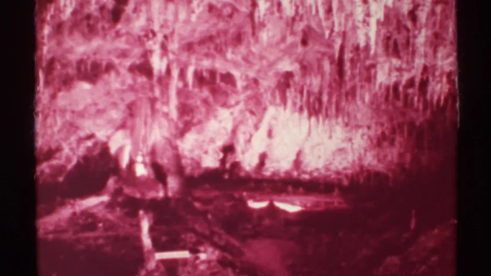 1972 New Mexico 8mm frame focused on red-tinted cave formations and rough cavern surfaces without a visible person.