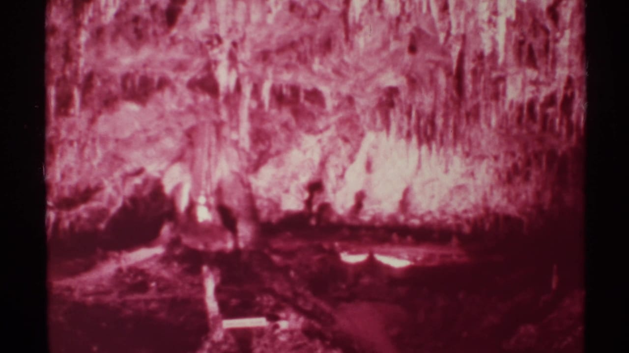 Red-tinted cave interior with stalactites, dark rock walls, and reflected light near the floor.
