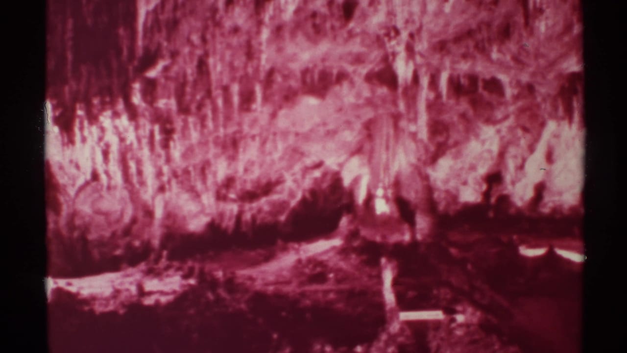 1972 New Mexico 8mm frame showing a pink monochrome cave interior with rough formations, bright highlights, and dark foreground shadows.