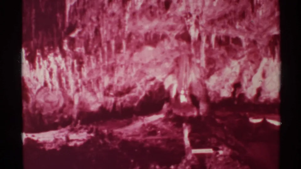 1972 New Mexico 8mm frame showing a pink monochrome cave interior with rough formations, bright highlights, and dark foreground shadows.