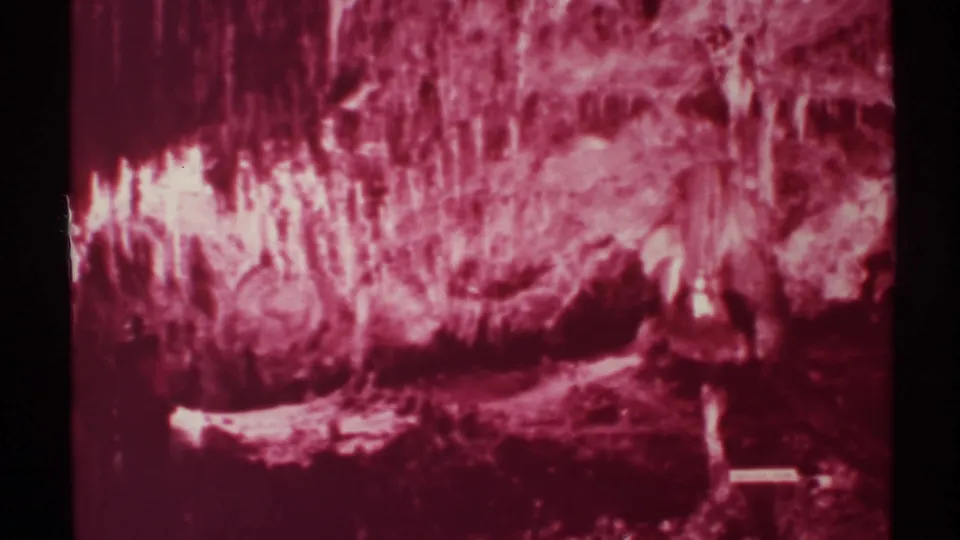 1972 New Mexico 8mm frame showing a soft, grainy cave view with bright mineral highlights on the left and a dark passage-like area below.